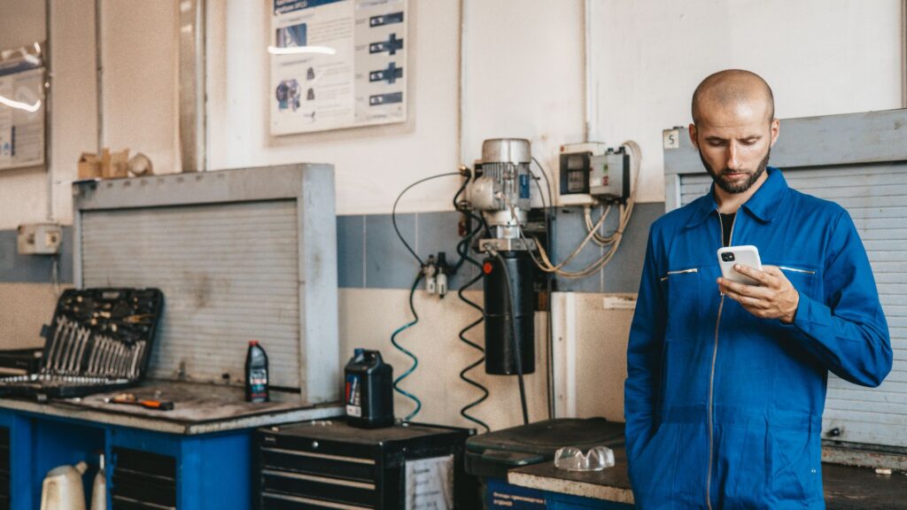 Handwerker in Arbeitskleidung schaut in der Werkstatt auf sein Smartphone