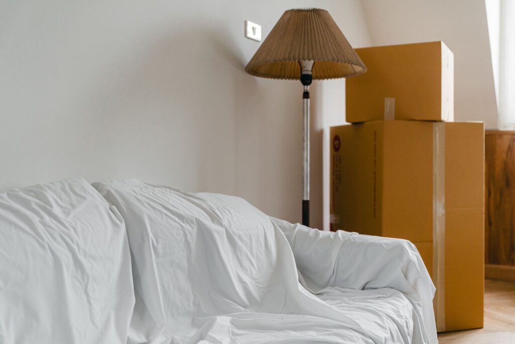 Leergeräumtes Wohnzimmer mit abgedecktem Sofa und gestapelten Kartons während einer Entrümpelung
