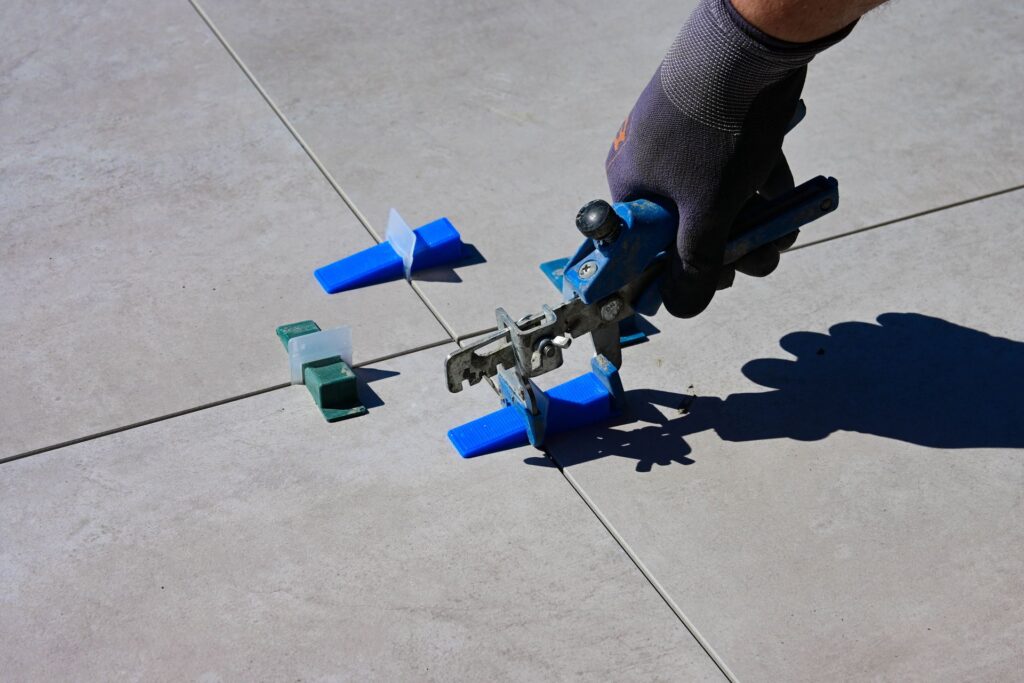 Hand mit Handschuh setzt Fliesen mit Abstandhaltern und Nivelliersystem