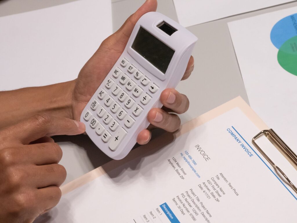 Hände prüfen eine Firmenrechnung mit einem Taschenrechner auf dem Schreibtisch